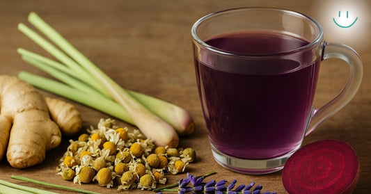 Glass mug of purple Tea For Life surrounded by ginger, chamomile, lemongrass, lavender, and beet root on a wooden table.